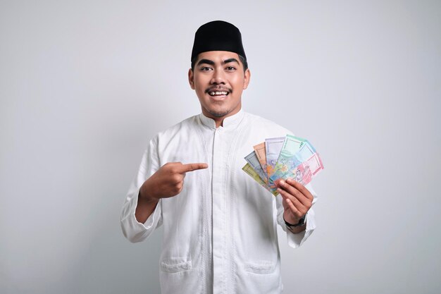 Foto homem muçulmano asiático sorridente em roupas brancas segurando papel de dinheiro rupiah
