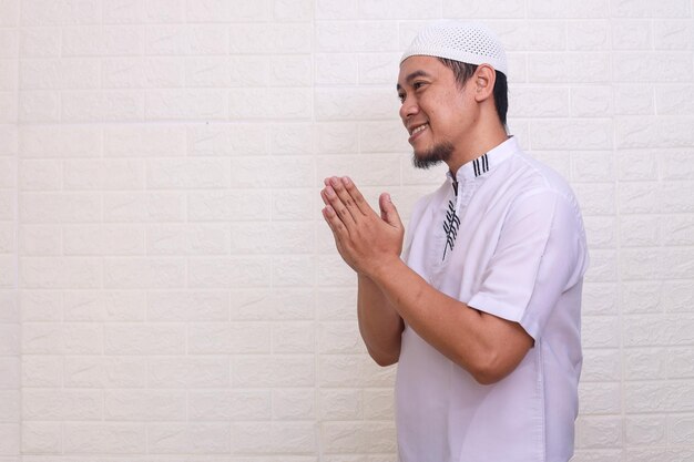 Homem muçulmano asiático sorridente gesticulando saudação de Eid Mubarak isolada sobre fundo branco