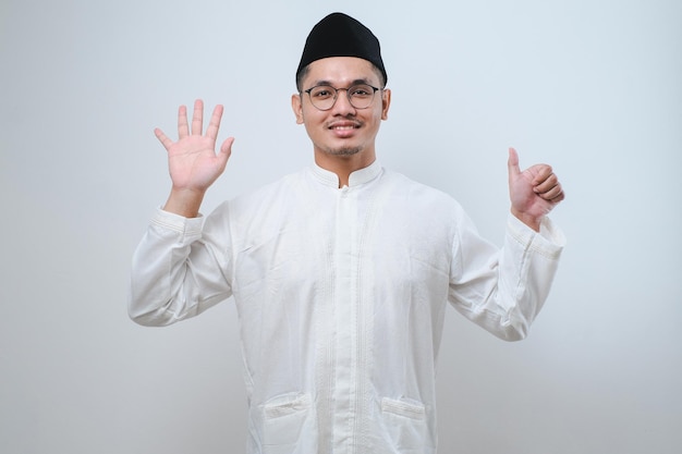 Homem muçulmano asiático vestindo roupas casuais mostrando e apontando para cima com os dedos número seis enquanto sorri confiante e feliz sobre fundo branco