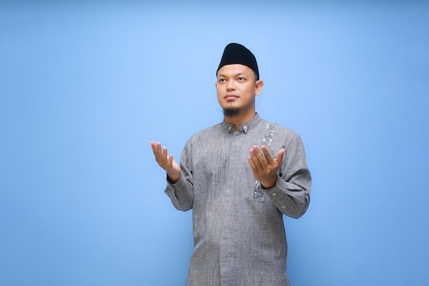 Foto homem muçulmano asiático vestindo roupas muçulmanas orando a deus isolado em fundo azul