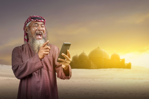 Homem muçulmano com barba usando keffiyeh com agal usando telefone celular