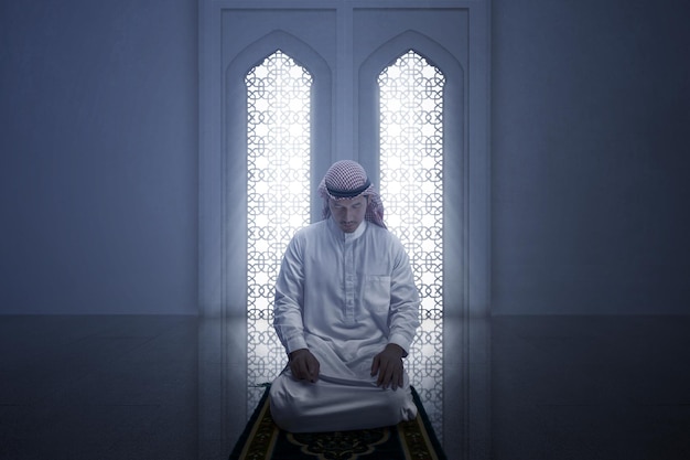 Homem muçulmano com keffiyeh com agal em posição de oração salat no tapete de oração