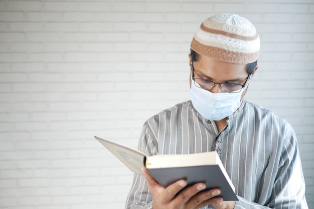 Homem muçulmano com máscara facial lendo livro de Alcorão.