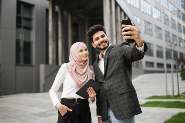 Homem muçulmano e mulher com roupa formal tomando selfie no celular