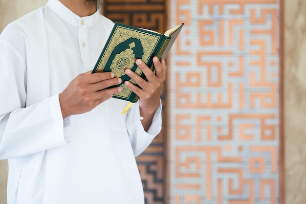 Homem muçulmano lendo o sagrado Alcorão Sagrado Alcorão na mão com o significado do texto em árabe do fundo do conceito islâmico Al Quran