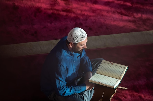 homem muçulmano rezando a Alá sozinho dentro da mesquita e lendo o livro sagrado islâmico Alcorão vista superior