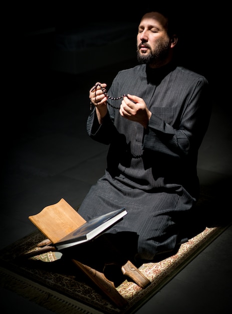 Homem muçulmano rezando por Deus no quarto escuro no Ramadã