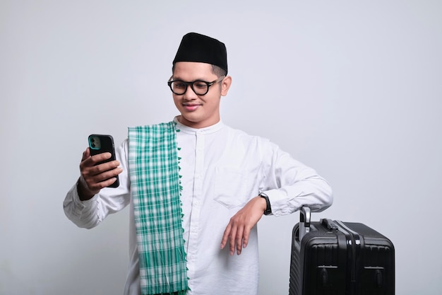 Foto homem muçulmano usando telefone celular enquanto se apoiava na mala preta pronta para o feriado eid mubarak