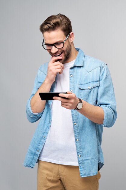 Homem muito casual com camisa jeans azul segurando o telefone em pé sobre a parede cinza do estúdio