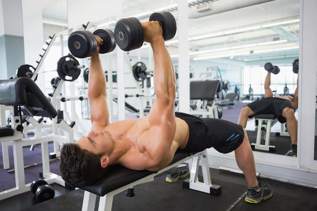 Homem muscular exercitando com dumbbells na academia