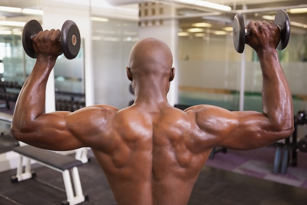 Homem muscular exercitando com dumbbells na academia