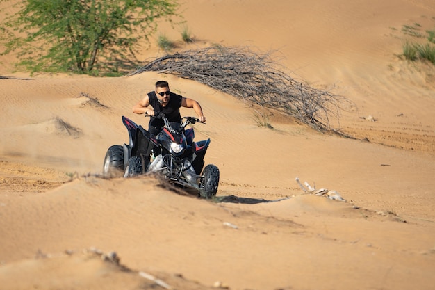 Homem musculoso, andando de quadriciclo no deserto.