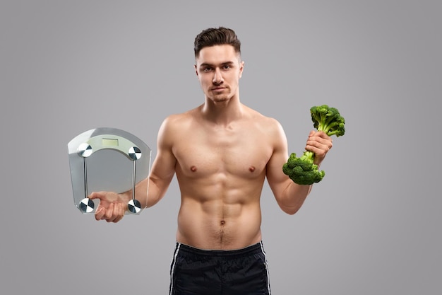 Homem musculoso apto carregando comida saudável e escalas