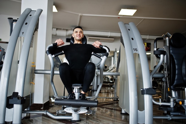 Homem musculoso árabe treinando e fazendo exercícios na máquina de fitness no ginásio moderno.