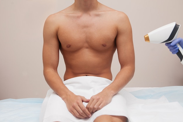 Homem musculoso atleta com pele clara suave. depilação e depilação de cabelos em salão de beleza. conceito de depilação a laser masculino. esteticista, usando aparelhos modernos para procedimentos. cuidados com a pele e beleza