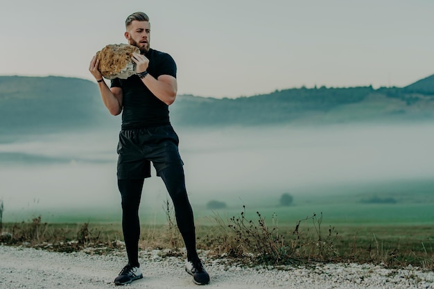 Homem musculoso atleta treina e exercita com pedra grande