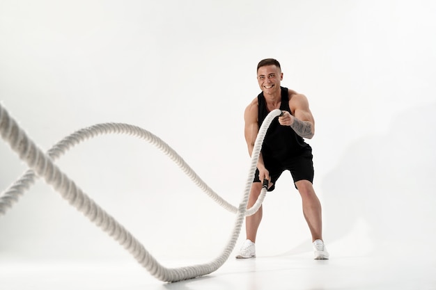 Homem musculoso atraente malhando com cordas pesadas. Foto de homem bonito em roupas esportivas isoladas em branco. Crossfit