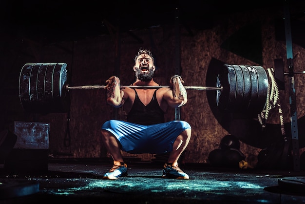 Homem musculoso barbudo tatuado fitness fazendo deadlift uma barra sobre a cabeça no moderno centro de fitness.