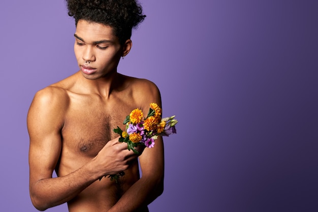 Homem musculoso com buquê de flores no fundo roxo. Retrato atirou em jovem hispânico atlético