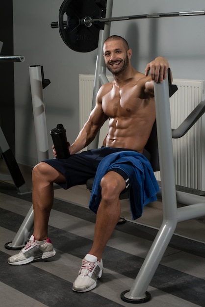 Homem musculoso descansando após o exercício e bebendo do shaker