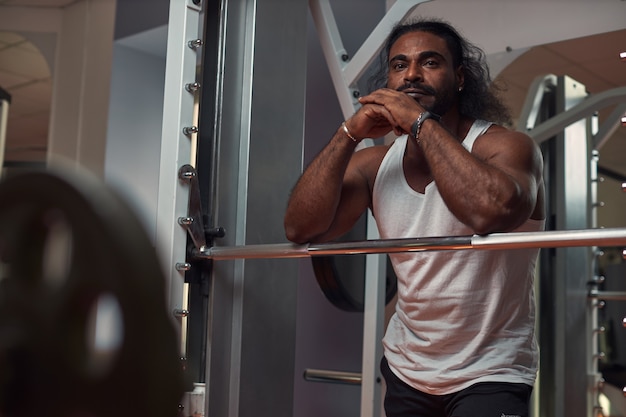 Foto homem musculoso e barbudo de cabelos compridos fica no ginásio perto do equipamento de exercício cara atraente com lo ...