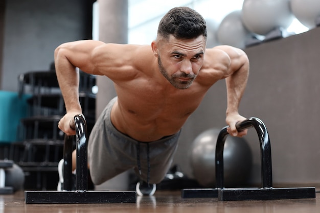 Homem musculoso e em forma, fazendo flexões horizontais com barras no ginásio.