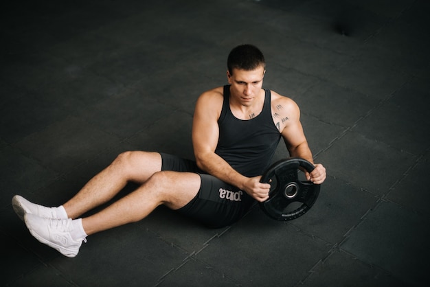 Homem musculoso e forte fazendo exercício de torção russa com peso na barra