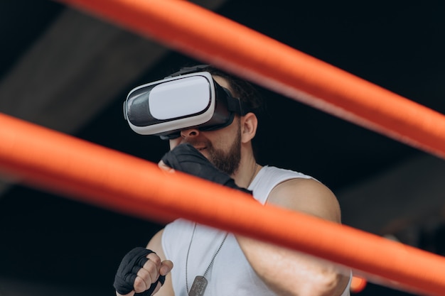 Homem musculoso em óculos de realidade virtual e luvas de boxe, dando socos em direção à câmera