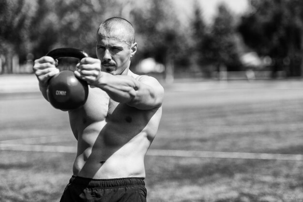 Homem musculoso exercitando com Kettlebell ao ar livre