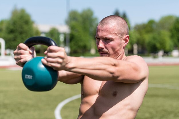 Homem musculoso exercitando com Kettlebell ao ar livre