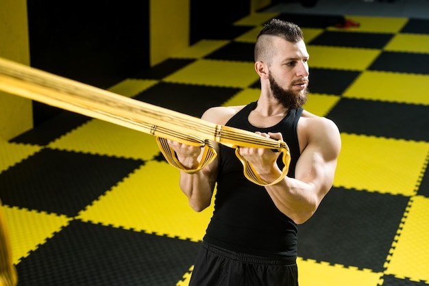 Homem musculoso faz exercícios com tiras de fitness no ginásio com interior preto e amarelo