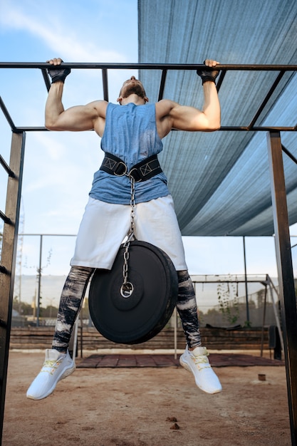 Homem musculoso fazendo exercícios de flexão com peso em uma barra horizontal