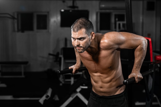 Homem musculoso fazendo flexões em barras desiguais no ginásio crossfit.