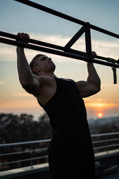 Homem musculoso fazendo flexões no conceito de fundo do céu ao pôr do sol de força de vontade, motivação e paixão