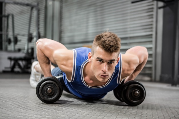 Homem musculoso fazendo push-up com halteres no ginásio crossfit