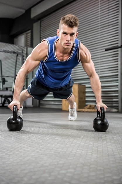 Homem musculoso fazendo push-up com kettlebells no ginásio crossfit