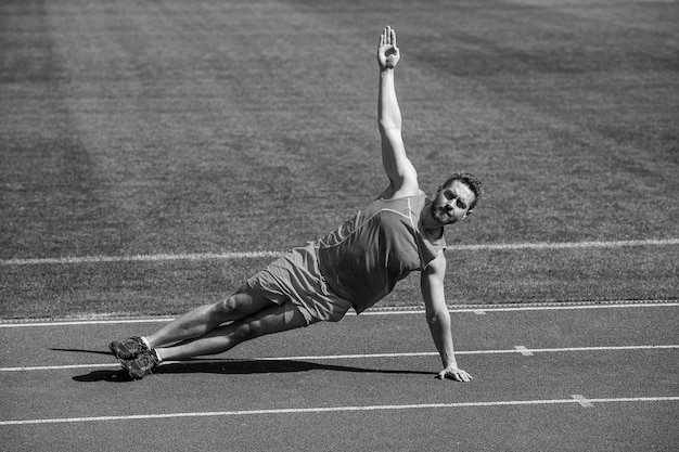 Homem musculoso fica na prancha lateral esticando na ioga de treinamento esportivo