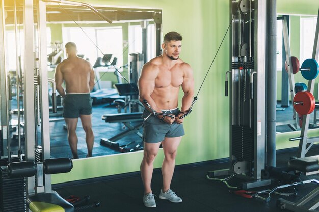 Homem musculoso malhando na academia fazendo exercícios no tríceps forte torso nu masculino