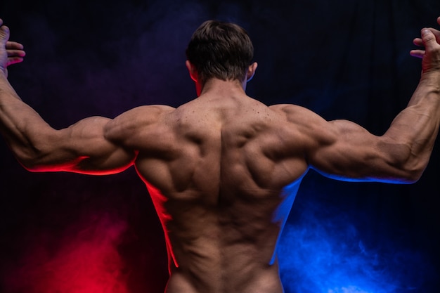 Homem musculoso mostrando músculos isolados no fundo preto com fumaça colorida