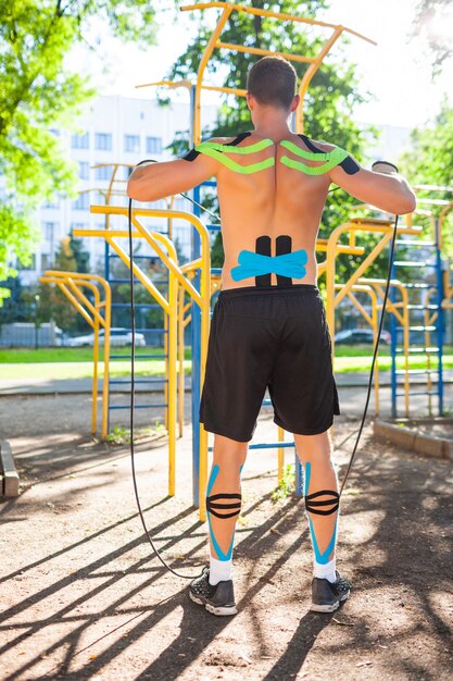 Homem musculoso nu treinando com corda de fitness em campo esportivo