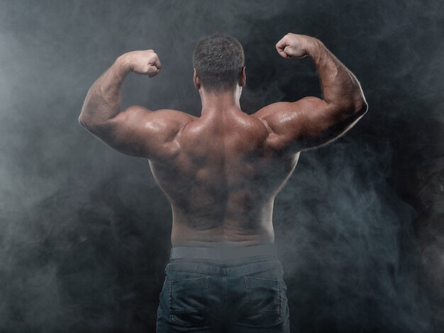 Homem musculoso poderoso mostra bíceps no preto. Conceito de força e fitness