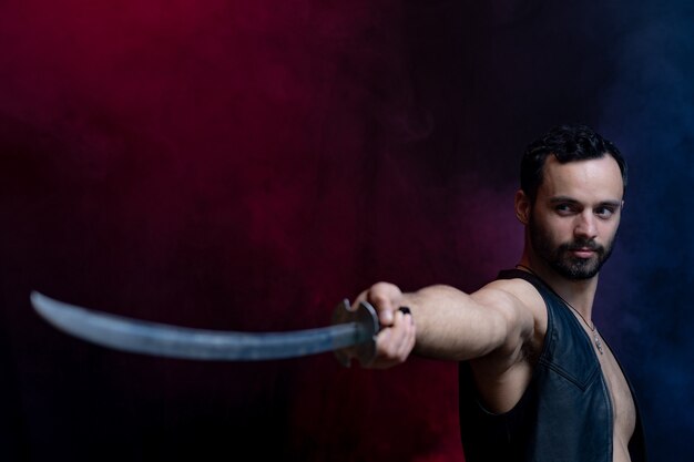 Homem musculoso posando com espada longa isolada em fundo preto e fumê