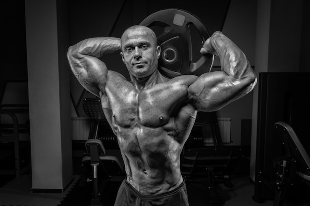 Homem musculoso, posando no ginásio com um disco de barra. conceito de musculação e levantamento de peso. mídia mista