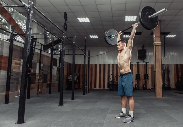 Homem musculoso praticando sobrecarga de peso pesado no health club moderno. Musculação e Fitness