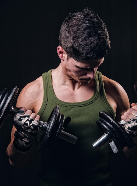 Homem musculoso segurando halteres contra um fundo preto