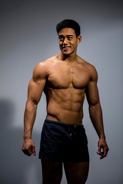 Homem musculoso sem camisa de pé contra um fundo cinzento