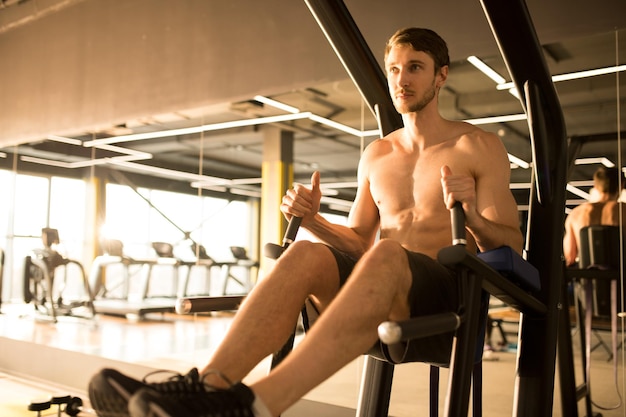 Homem musculoso sem camisa fazendo exercícios na máquina de fitness no ginásio