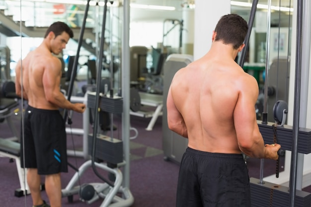 Homem musculoso sem camisa usando tríceps puxa para baixo na academia