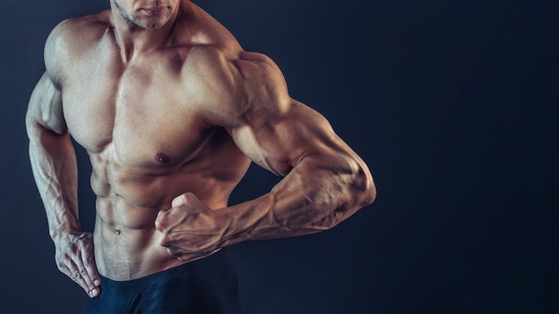Homem musculoso sexy, atlético forte e irreconhecível se equilibrando, mostrando bíceps e deltóides no espaço negro