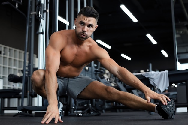 Homem na academia fazendo exercícios de alongamento no chão.